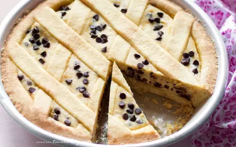 Deliziosa torta ricotta e cioccolato con decorazione a griglia e gocce di cioccolato. Una fetta è stata tolta, rivelando il ripieno cremoso.