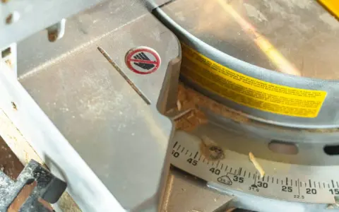 Detalle de una sierra ingletadora con marcas de ángulo para saber como medir para cortar a inglete. Se ve serrín y una advertencia de seguridad.