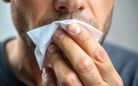 Mężczyzna wyciera nos chusteczką. Czy to przeziębienie, czy może alergia? Ten **slinotok od czego** może być uciążliwy.