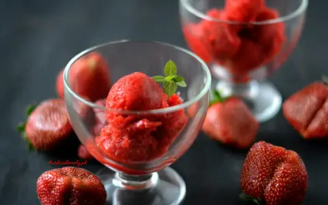 Orzeźwiający sorbet truskawkowy w pucharkach, otoczony świeżymi truskawkami. Idealny deser na upalne dni.