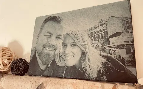 Foto piedra con retrato de pareja sonriente, con edificios y un puesto de helados al fondo.
