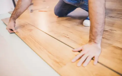 Mann verlegt Laminat. Die Holzoptik der Dielen wird sorgfältig zusammengefügt.