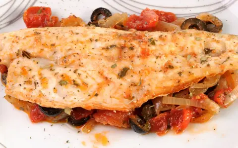 Leckerer Barsch zubereitet mit Tomaten, Zwiebeln und Oliven, garniert mit Kräutern. Ein Genuss für jeden Fischliebhaber.