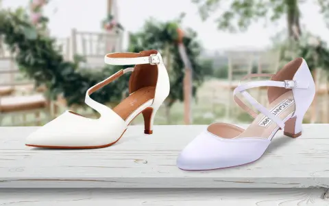 Due eleganti scarpe da sposa bianche, una con cinturino alla caviglia, l'altra con incroci sul collo del piede, su un tavolo di legno con sfondo sfocato di un matrimonio.