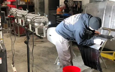 A person in a garage works on a car part, learning how to buff it to a shine.