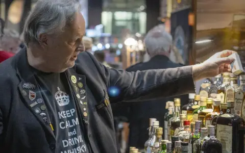 Mann mit "Keep Calm and Drink Whisky"-Shirt und vielen Ansteckern auf einer Whiskey Messe, der eine kleine Box hält.