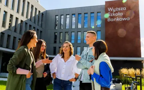 Grupa studentów śmieje się przed budynkiem Wyższej Szkoły Bankowej w Sosnowcu.