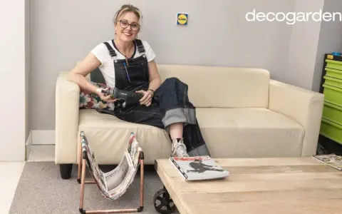 Mujer con overol sentada en sofá beige, sosteniendo una herramienta. A su lado, un revistero diy hecho con cobre y tela.