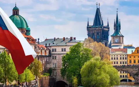 Flaga Czech powiewa nad Pragą, ukazując ciekawe fakty o Czechach. W tle widać Most Karola i wieże.