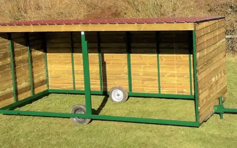 Abri pour chevaux en bois, mobile et sans permis de construire, avec toit rouge et structure verte.
