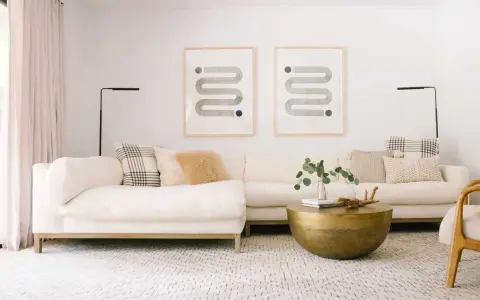 En ljus soffgrupp med en mönstrad matta och ett runt soffbord i mässing. Två grafiska tavlor hänger på väggen.