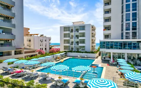 Albania - wczasy samolotem all inclusive. Basen hotelowy z leżakami i parasolami, w tle budynki i morze. Idealne miejsce na relaks.
