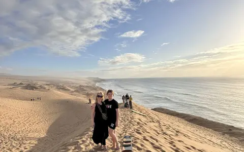 Dwie kobiety na wydmach nad oceanem, w tle inni turyści. Czy w Maroko jest bezpiecznie dla turystów? Tak, to piękny kraj.