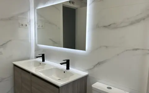 Moderno lavabo doble con grifería negra y espejo iluminado. Una solución ideal para reformar baño sin obras, con un toque de elegancia.