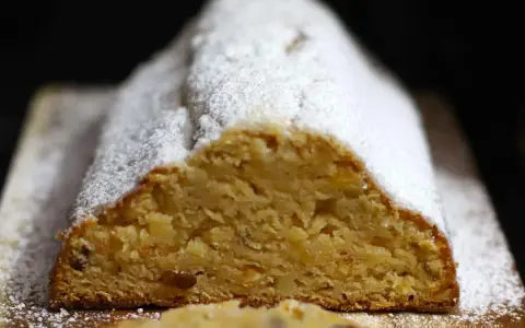 Ein saftiger Quarkstollen mit Marzipan, bestäubt mit Puderzucker, wartet auf den Anschnitt.