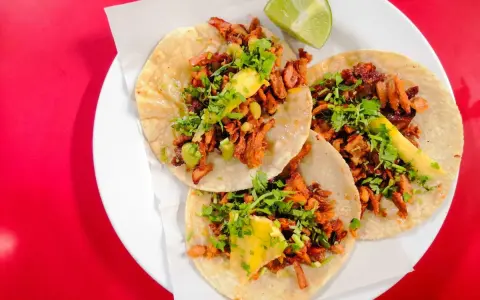 Tres deliciosos tacos al pastor, con cilantro, piña y un toque de limón, listos para disfrutar.