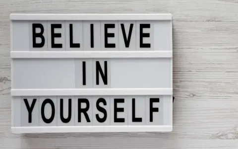 Biała tablica z czarnymi literami: "BELIEVE IN YOURSELF". To przesłanie inspiruje do nastawienia na rozwój i wiary we własne możliwości.