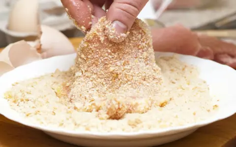 Fleisch wird in Paniermehl gewendet. Eine Hand hält das Stück, um es perfekt panieren ohne Ei zu machen.