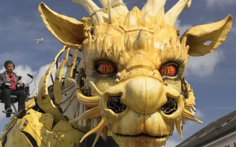 Ein Mann steuert eine riesige Holzdrachen-Skulptur, deren Augen bedrohlich glühen. Die Szene wirkt wie eine Warnung vor drakonischen Strafen, während ein Flugzeug am Himmel vorbeizieht.