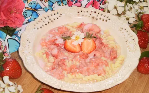 Makaron fusilli z sosem truskawkowym, udekorowany połówkami truskawek i kwiatkiem.