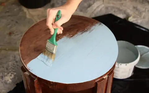 Mano aplicando pintura a la tiza color madera a una mesa redonda.
