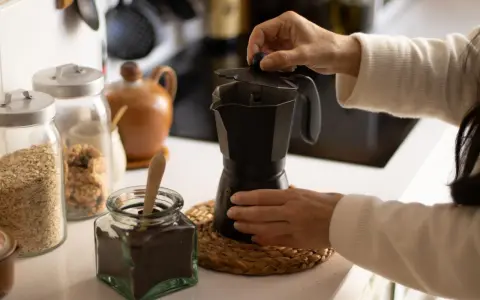 Manos preparando un café con alcohol en cafetera italiana. Hay frascos con avena y café molido.