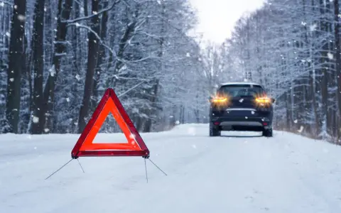 Warnblinkleuchten und Warndreieck auf verschneiter Straße. Ein Auto steht im Hintergrund. Ein wichtiger Hinweis für den auto wintercheck.