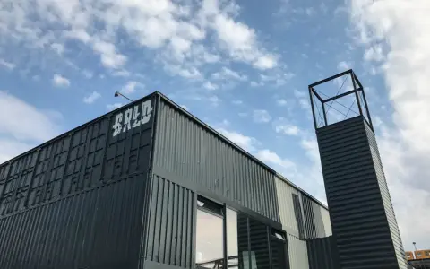 Moderne Containerarchitektur am **brlo gleisdreieck** mit Schriftzug "BALD" und einem markanten Turm unter blauem Himmel.