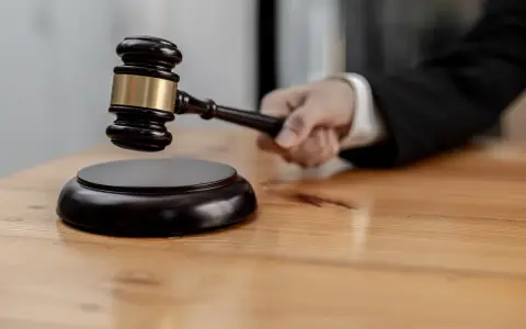 Mano che impugna un martelletto da giudice, pronto a battere sul ceppo. Il suo significato, il g.u.p., è un momento cruciale.