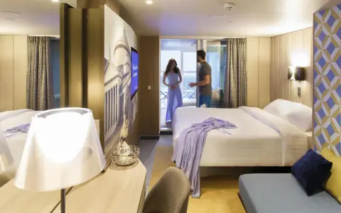 Coppia in una moderna cabina interna di Costa Crociere. Letto matrimoniale, decorazioni artistiche e un balcone invitano al relax.