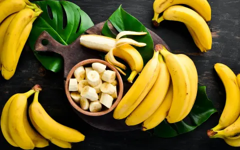 Pęki dojrzałych bananów, jeden obrany i pokrojony w miseczce. Zastanawiasz się, ile węglowodanów ma banan?