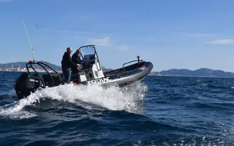 Deux hommes en Zodiac effectuent une navigation mer, projetant des embruns sous un ciel bleu.