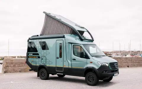 En grön Hymer Venture S husbil med uppfällt tak står parkerad vid en hamn.