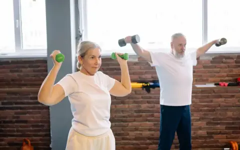 Mujer de 50 años tonifica sus brazos con mancuernas verdes. Un hombre a su lado también entrena.