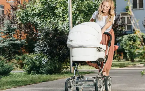 Uśmiechnięta mama spaceruje z białym wózkiem, który jest wyposażony w praktyczne akcesoria.