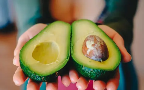 Zwei Hälften einer Avocado werden in Händen gehalten. Eine Hälfte hat den Kern, die andere ist leer. Perfekt, um die Avocado reifen zu lassen.