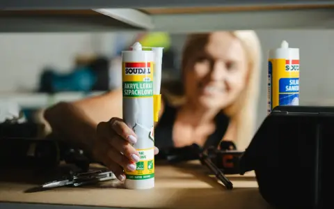 Kobieta trzyma tubkę akrylu lekkiego szpachlowego Soudal. Po jakim czasie można malować akryl? Po wyschnięciu i zeszlifowaniu.