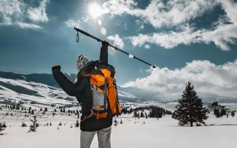 Osoba z plecakiem wznosi kijek, przygotowując się do marszu. Dowiedz się, jak prawidłowo założyć buciki na kijki nordic walking, by cieszyć się zimową wędrówką.