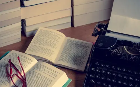 Stos książek, otwarta księga z okularami i zabytkowa maszyna do pisania. Idealne miejsce do tworzenia streszczeń i pisania.