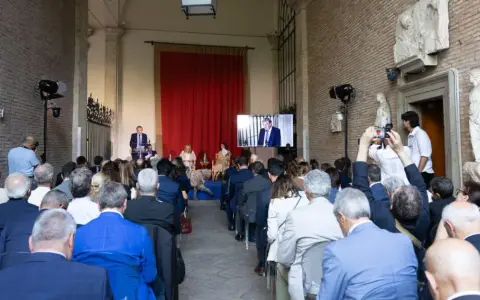 Un evento per il meeting per l'amicizia fra i popoli. Un relatore parla a un pubblico seduto, mentre un altro viene trasmesso su uno schermo.