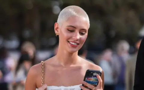 Junge Frau mit buzz cut blond, lächelnd und auf ihr Handy schauend.