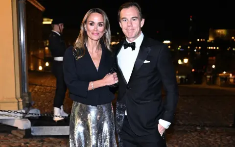 A couple in formal attire poses at night with a blurred city background.