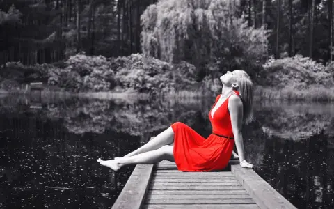 Mujer con vestido rojo sentada en muelle, efecto blanco y negro photoshop.