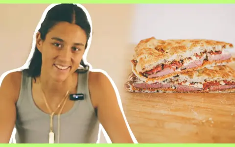 Mujer sonriente junto a un pepito de ternera cortado en dos, mostrando el relleno de carne, queso y pimientos.