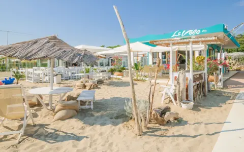 Un angolo di cervia strand con tavoli, sedie e ombrelloni di paglia, pronto ad accogliere i bagnanti.