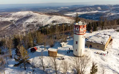 Wieża widokowa na Biskupiej Kopie w zimowej scenerii. Śnieg otula zbocza i drzewa, a budynki tworzą malowniczy krajobraz.