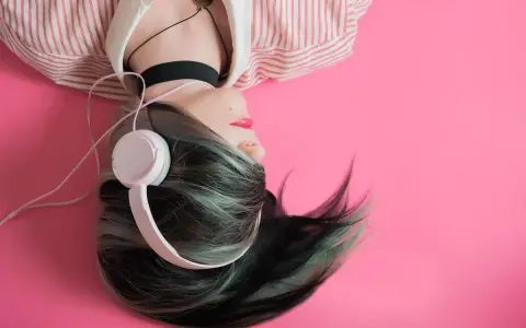 Jeune femme aux cheveux colorés, écouteurs blancs, sur fond rose. Une inspiration pour comment trouver un nom d'artiste.