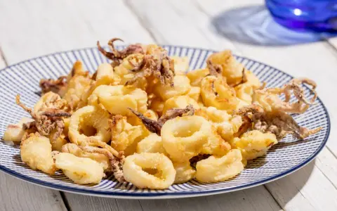 Calamari croccanti e dorati, cotti alla perfezione nella friggitrice ad aria, serviti su un piatto a righe blu.
