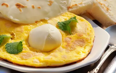 Frittata soffice con mozzarella filante, guarnita con foglie di menta fresca. Accompagnata da fette di pane tostato.