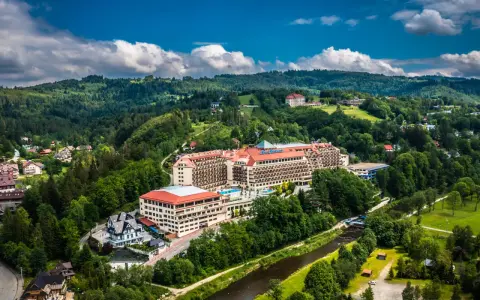 Widok z lotu ptaka na duży hotel Gołębiewski otoczony zielonymi wzgórzami i rzeką.